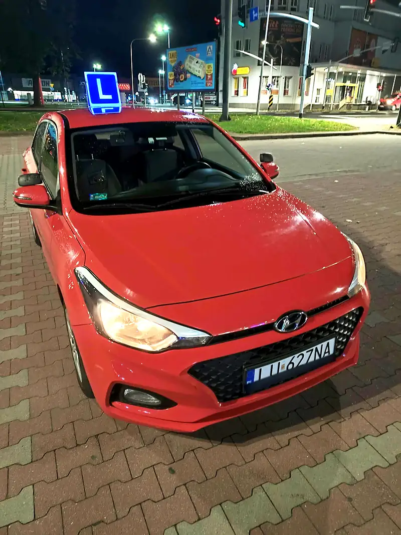 Czerwony Hyundai i20 Viral OSK z oznaczeniem L wieczorem w mieście